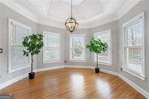 unfurnished dining area with ornamental molding, a chandelier, wood finished floors, coffered ceiling, and baseboards