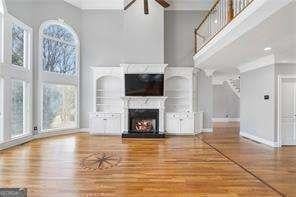 unfurnished living room featuring ceiling fan, a high ceiling, a lit fireplace, and wood finished floors