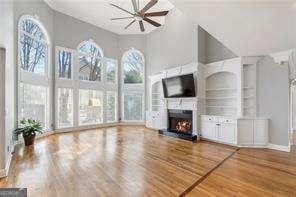 unfurnished living room with a towering ceiling, ceiling fan, wood finished floors, and a warm lit fireplace