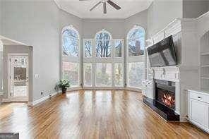 unfurnished living room featuring a wealth of natural light, a lit fireplace, wood finished floors, and ceiling fan