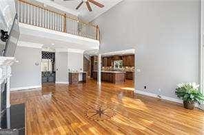 unfurnished living room with ceiling fan, a fireplace, a high ceiling, wood finished floors, and baseboards