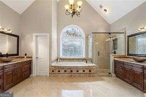 full bath with two vanities, high vaulted ceiling, an inviting chandelier, a bath, and a stall shower