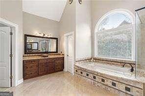 bathroom featuring a wealth of natural light, vanity, a bath, and high vaulted ceiling