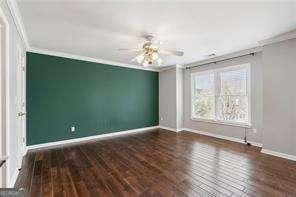 unfurnished room featuring crown molding, wood finished floors, baseboards, and a ceiling fan