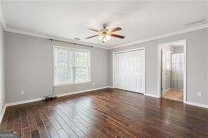 unfurnished bedroom featuring a closet, baseboards, ceiling fan, crown molding, and wood finished floors