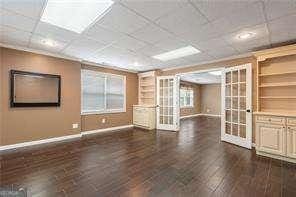 empty room featuring french doors, baseboards, built in shelves, and dark wood finished floors