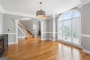 unfurnished dining area featuring arched walkways, wood finished floors, stairs, baseboards, and a notable chandelier