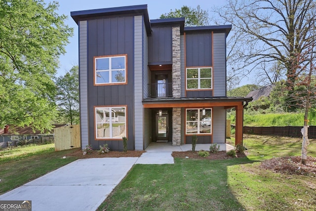 modern home featuring a front yard, a balcony, board and batten siding, and fence