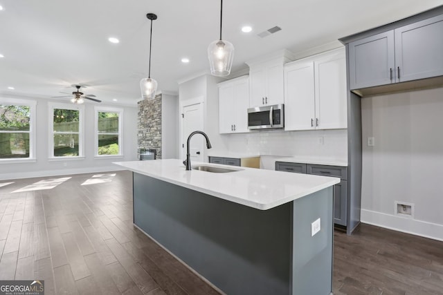 kitchen featuring a sink, a ceiling fan, stainless steel microwave, dark wood-type flooring, and pendant lighting