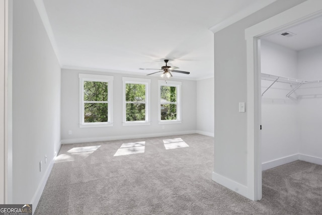 interior space with crown molding, a ceiling fan, carpet flooring, a walk in closet, and baseboards