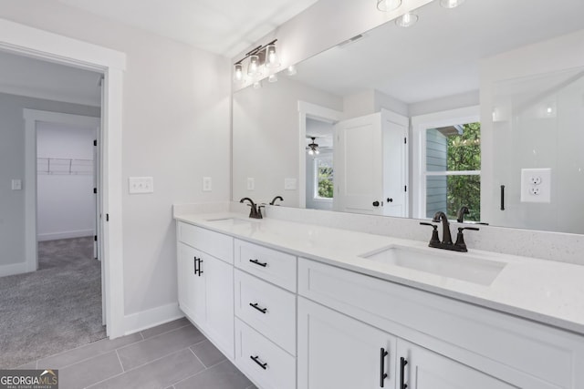 full bathroom with a walk in closet, double vanity, baseboards, and a sink