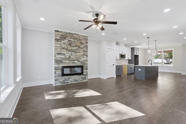 unfurnished living room featuring crown molding, dark wood finished floors, a ceiling fan, and a stone fireplace