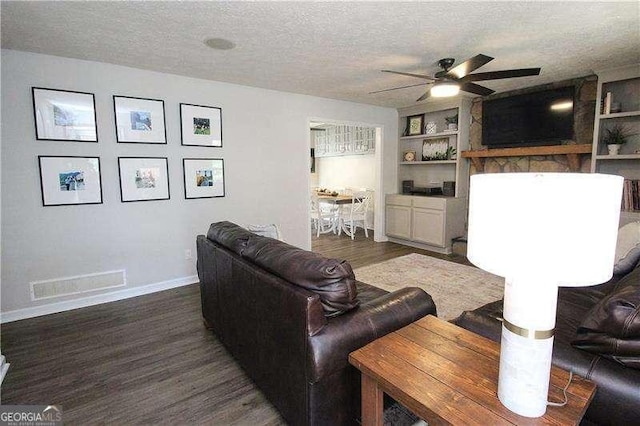 living room with a textured ceiling, visible vents, baseboards, wood finished floors, and a ceiling fan