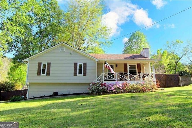 view of front of property with a chimney, fence, a porch, and a front lawn
