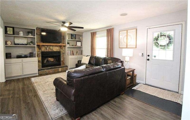 living area with a textured ceiling, built in shelves, ceiling fan, a fireplace, and dark wood-style flooring