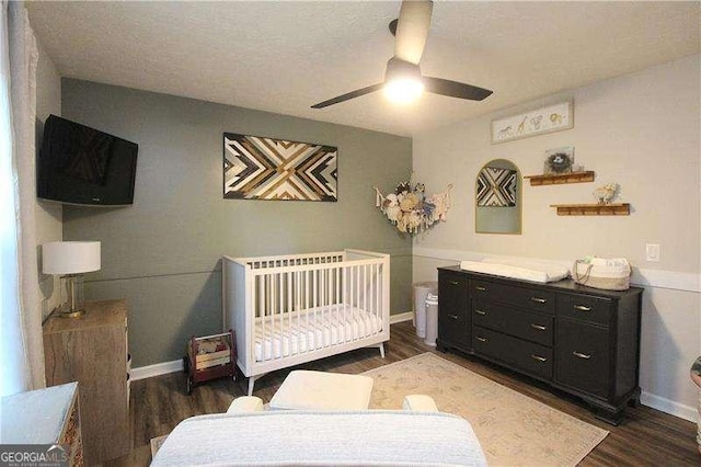 bedroom with a nursery area, wood finished floors, baseboards, and ceiling fan