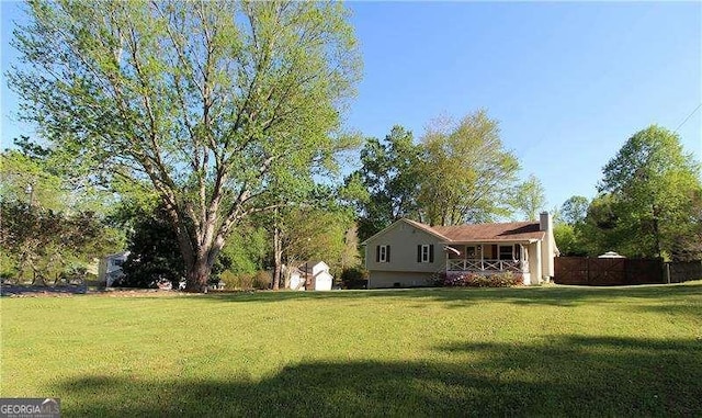view of yard featuring a storage unit, a porch, and fence