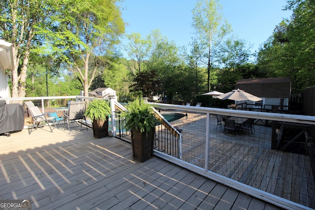 wooden terrace featuring an outdoor structure, an outdoor pool, area for grilling, and a shed