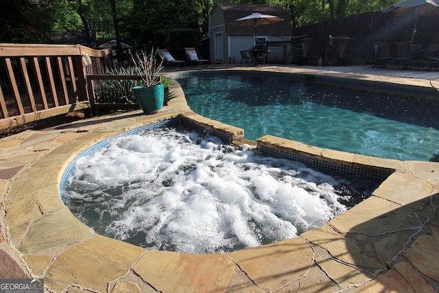 outdoor pool featuring fence, an outbuilding, and an in ground hot tub