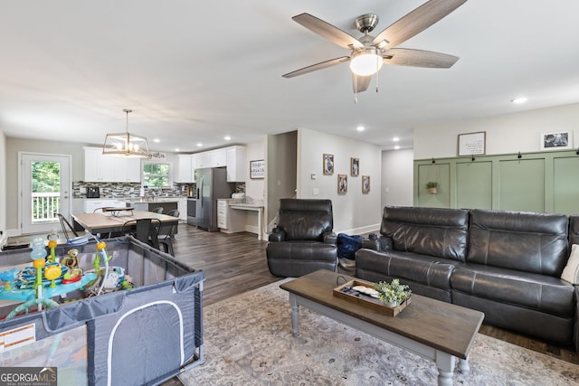 living room featuring ceiling fan with notable chandelier, recessed lighting, and dark wood-style flooring