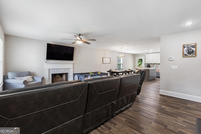 living area featuring baseboards, ceiling fan, a fireplace, recessed lighting, and dark wood-type flooring