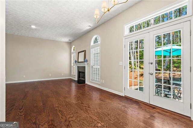 unfurnished living room with a fireplace, a textured ceiling, wood finished floors, french doors, and baseboards