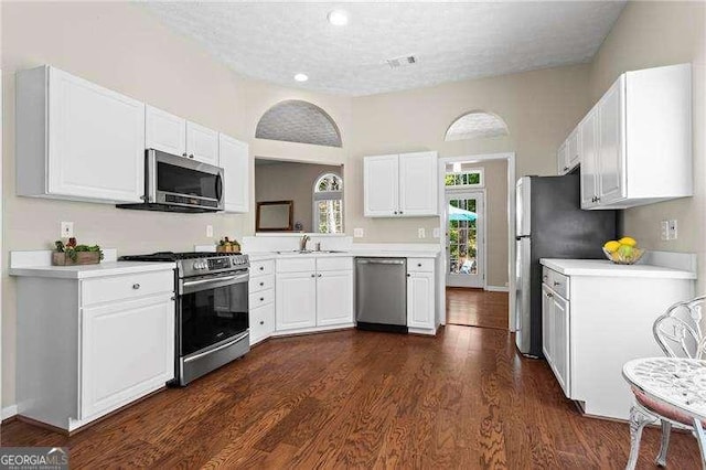 kitchen featuring white cabinets, appliances with stainless steel finishes, dark wood-style flooring, light countertops, and a sink