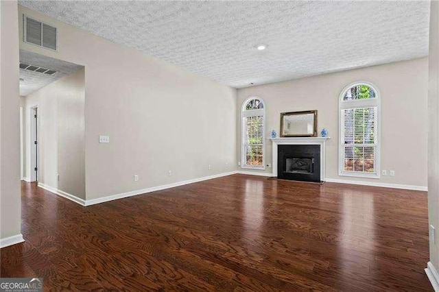 unfurnished living room with baseboards, a textured ceiling, a fireplace with flush hearth, visible vents, and wood finished floors