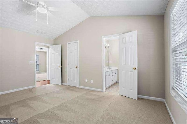 unfurnished bedroom featuring baseboards, ceiling fan, ensuite bath, vaulted ceiling, and light carpet