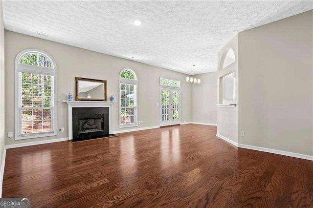 unfurnished living room with baseboards, an inviting chandelier, a fireplace, a textured ceiling, and wood finished floors