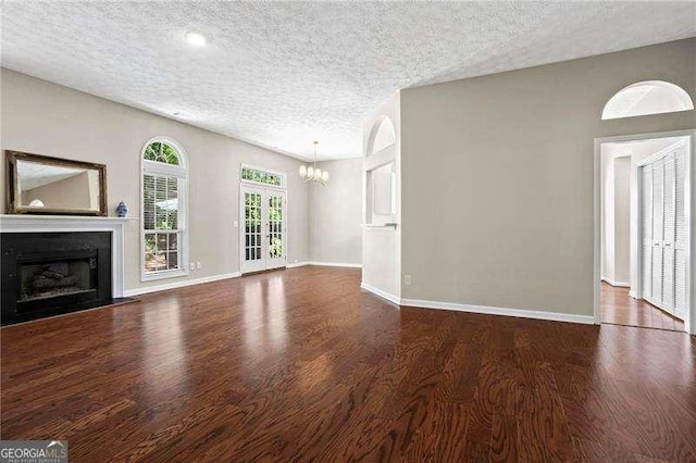 unfurnished living room with a chandelier, a textured ceiling, and wood finished floors