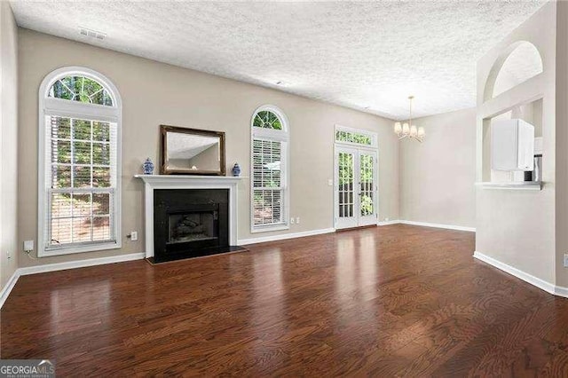 unfurnished living room featuring a fireplace with flush hearth, a notable chandelier, wood finished floors, and a textured ceiling