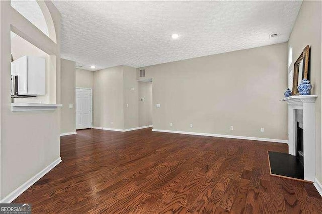 unfurnished living room featuring a fireplace, a textured ceiling, baseboards, and wood finished floors