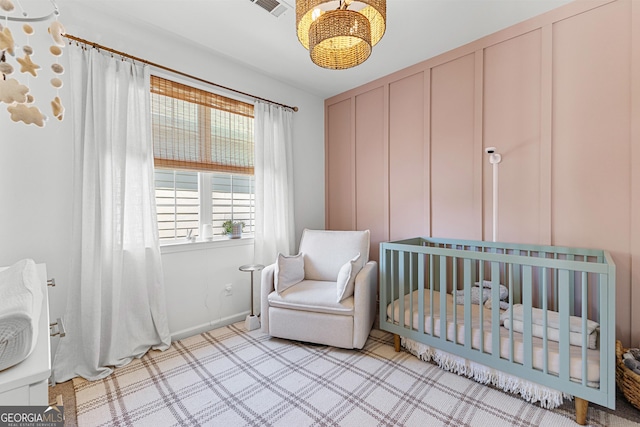 bedroom featuring a decorative wall, an inviting chandelier, a nursery area, visible vents, and carpet floors