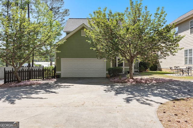 view of side of home with concrete driveway, a shingled roof, fence, and an attached garage