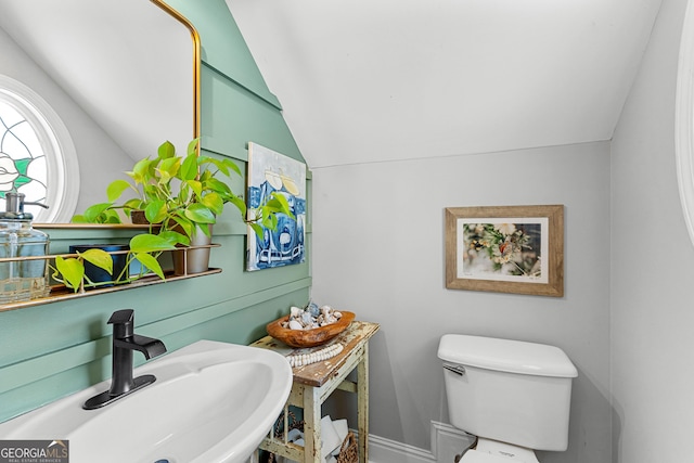 half bathroom featuring toilet, baseboards, a sink, and vaulted ceiling