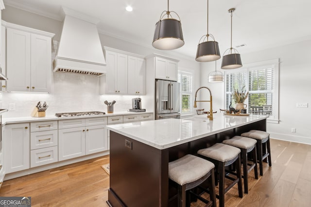 105 Whispering Oaks Ln, Saint Marys, GA 31558 - kitchen featuring custom range hood, light wood-style floors, a center island with sink, decorative backsplash, and stainless steel appliances