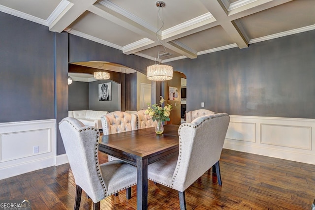dining space with arched walkways, a decorative wall, hardwood / wood-style floors, beam ceiling, and coffered ceiling