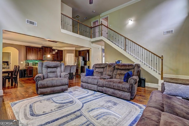 living area featuring a high ceiling, wood finished floors, ornamental molding, and visible vents