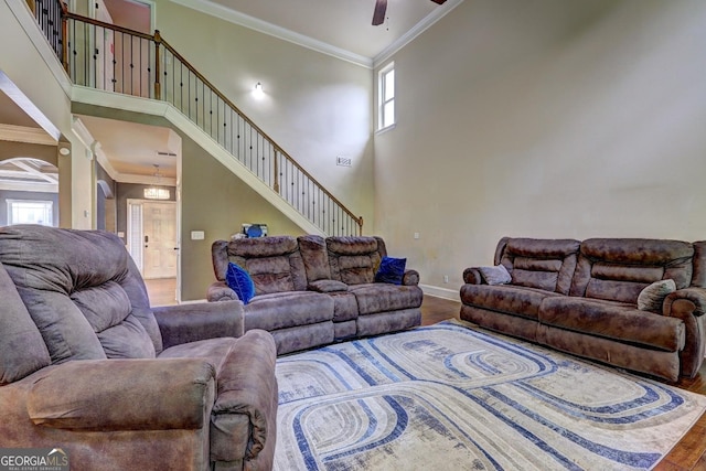 living room featuring a towering ceiling, a ceiling fan, ornamental molding, wood finished floors, and baseboards
