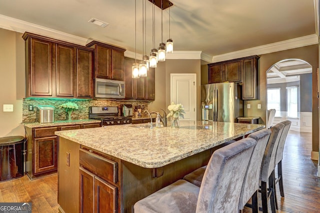 kitchen featuring ornamental molding, appliances with stainless steel finishes, arched walkways, and hardwood / wood-style floors