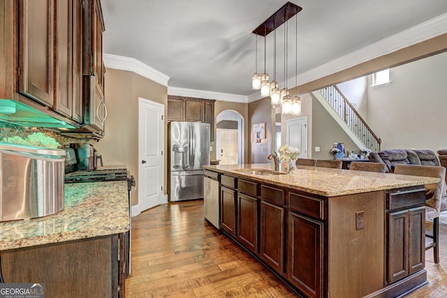 kitchen featuring appliances with stainless steel finishes, an island with sink, dark wood finished floors, pendant lighting, and a sink
