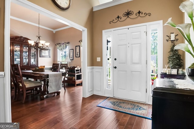 entrance foyer with ornamental molding, an inviting chandelier, dark wood-style floors, and a wealth of natural light
