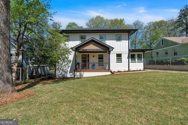 back of house featuring board and batten siding, fence, covered porch, and a lawn