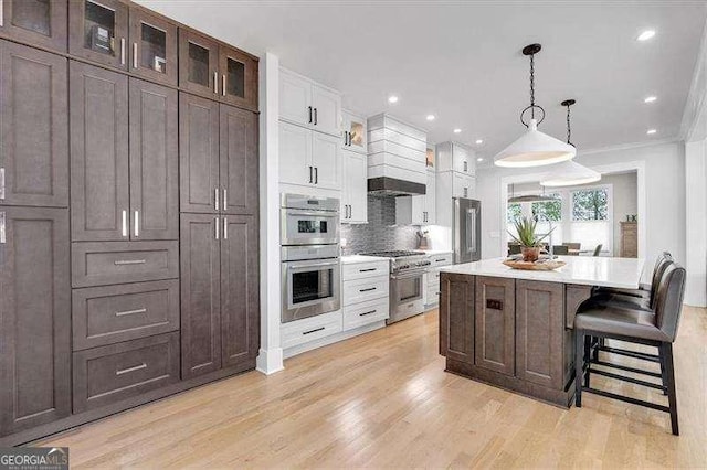 kitchen featuring white cabinets, light countertops, premium range hood, high quality appliances, and light wood finished floors