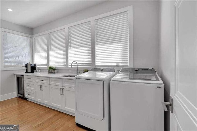 washroom featuring light wood-type flooring, a sink, washer and dryer, wine cooler, and cabinet space