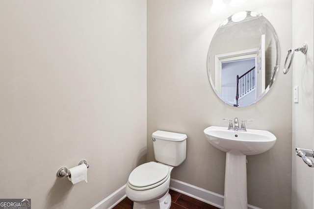 half bath with toilet, wood finished floors, a sink, and baseboards