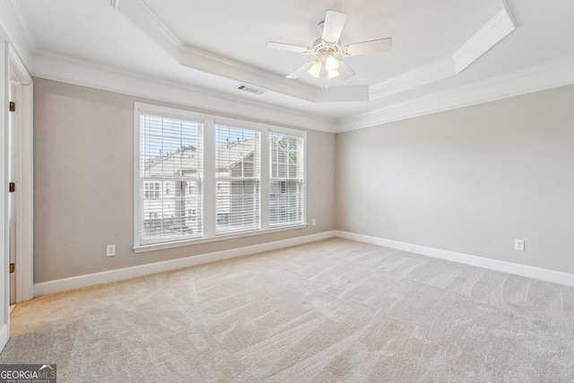 empty room featuring a tray ceiling, light colored carpet, ornamental molding, and visible vents