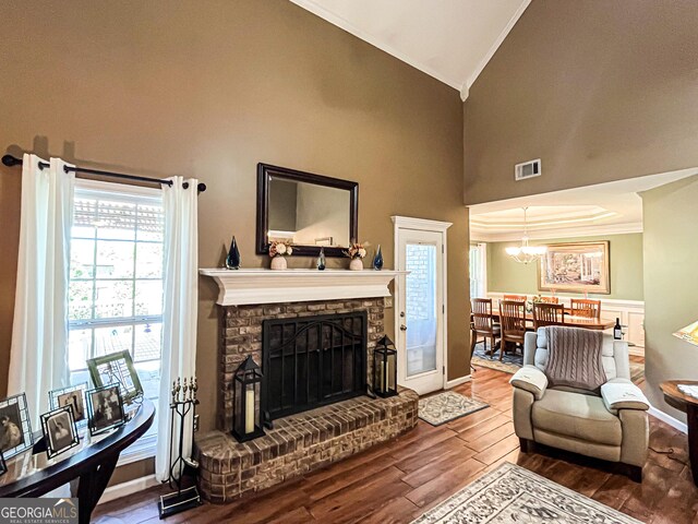 living room with crown molding, a fireplace with raised hearth, visible vents, a chandelier, and wood finished floors