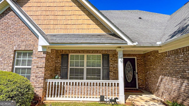 view of exterior entry featuring brick siding, a shingled roof, and covered porch